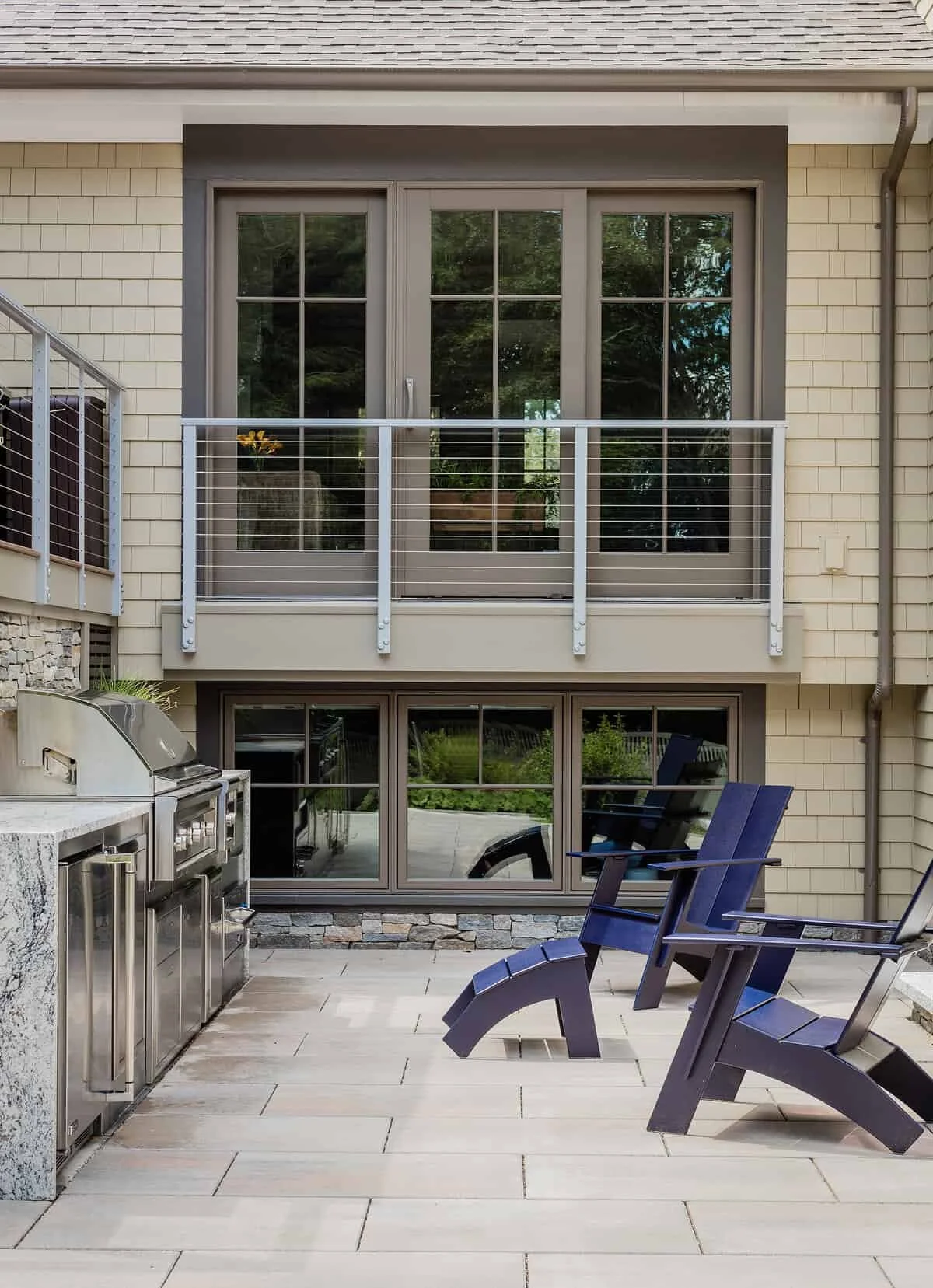 Outdoor patio with beige tile flooring, blue lounge chairs, a built-in grill, and sliding glass doors leading into a house