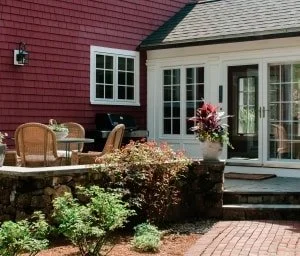 A backyard patio with outdoor furniture and a flower arrangement in front of a house with red siding and white trim.