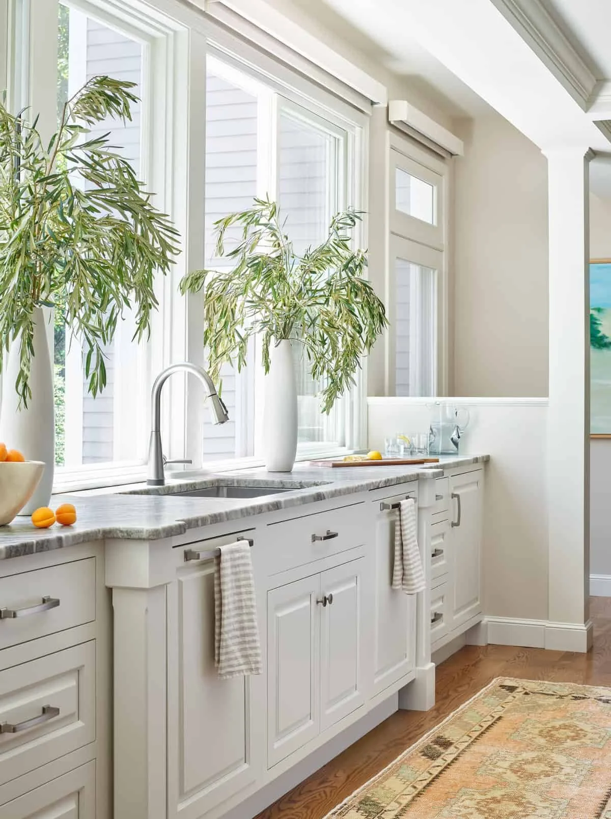 Bright kitchen with white cabinetry, a marble countertop, large window with natural light, and decorative plants on the counter.