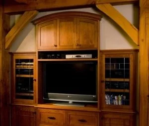 Wooden entertainment center with a large TV, shelves on either side with books and decorative items, and a cabinet above the TV.