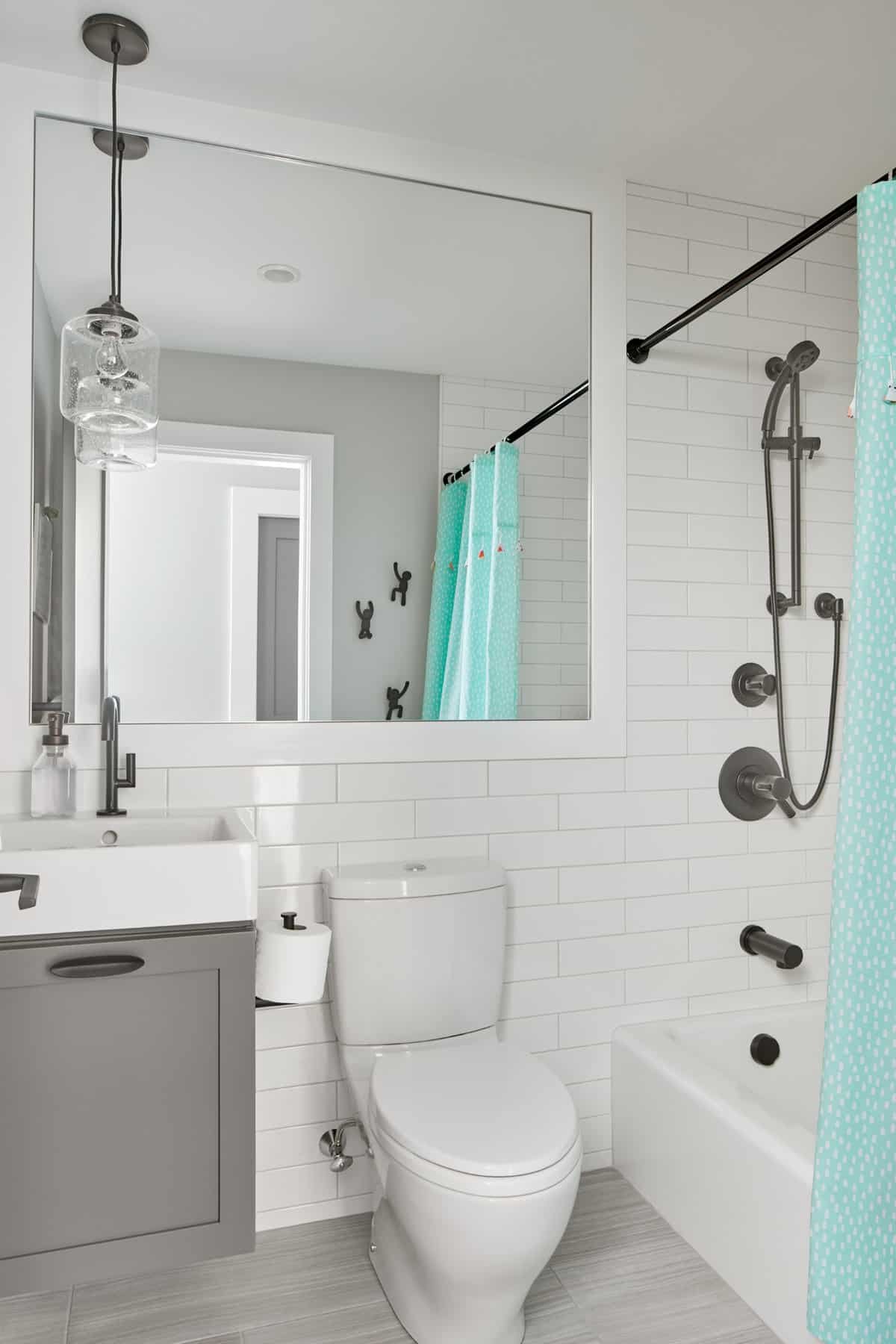 Modern bathroom with white subway tile walls featuring black fixtures, including a showerhead and faucet, a mirror above a gray vanity, a toilet, and a bathtub with a teal shower curtain.