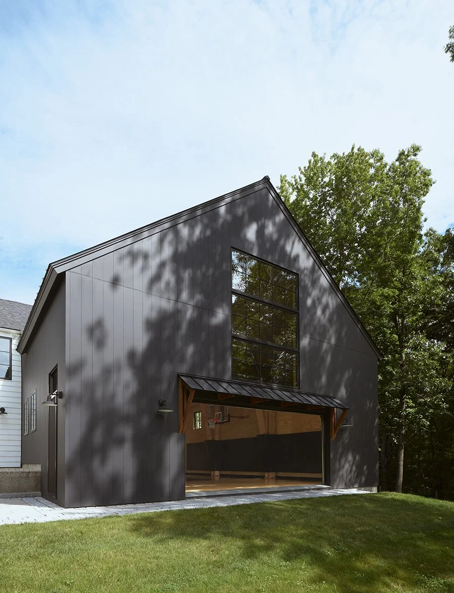 Modern black detached garage with large windows and an overhang, adjacent to a green lawn with trees in the background.