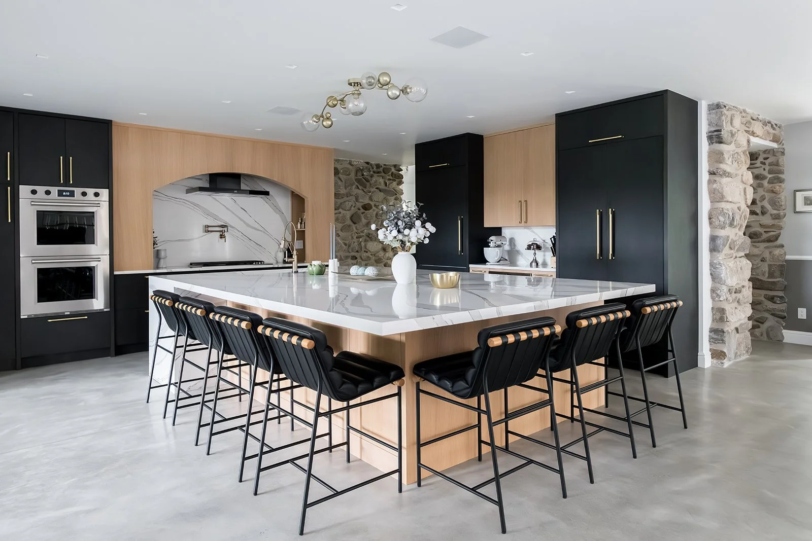 Modern kitchen with black and wood cabinetry, marble island, stone accent wall, and stainless steel appliances.
