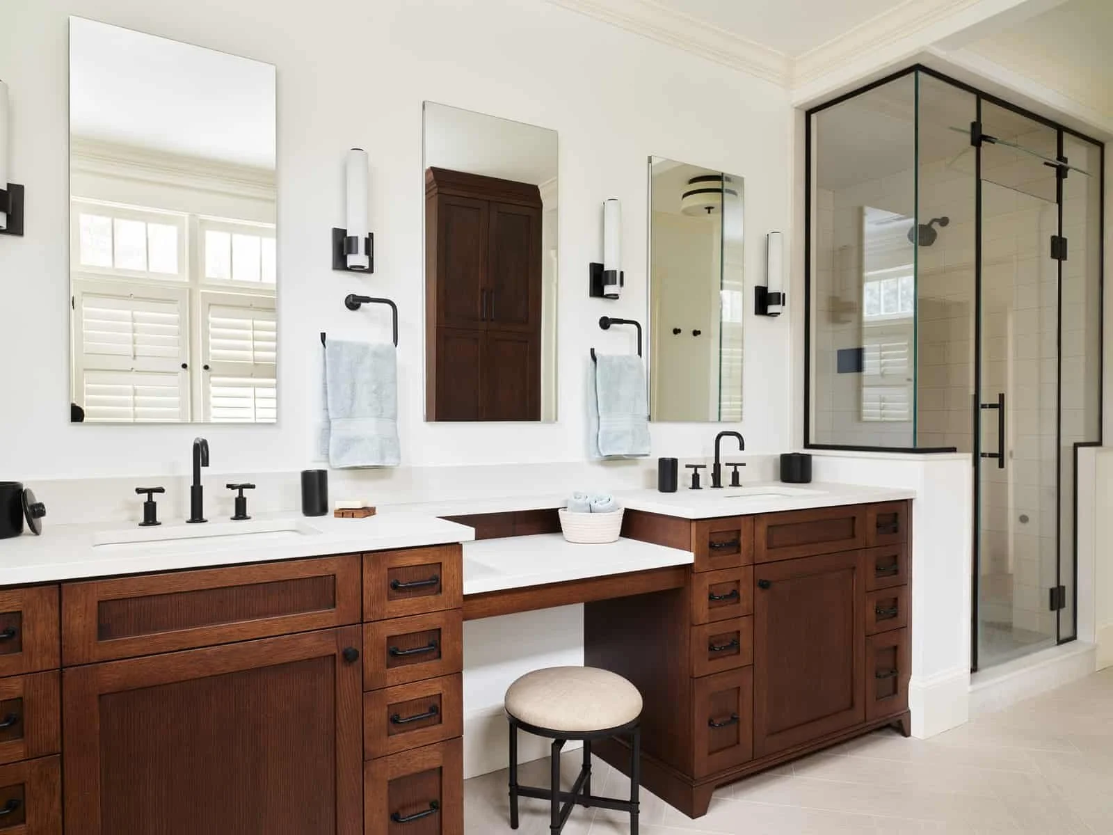 A modern bathroom with a double vanity featuring wooden cabinets, large mirrors, black fixtures, and a walk-in shower with glass enclosure.