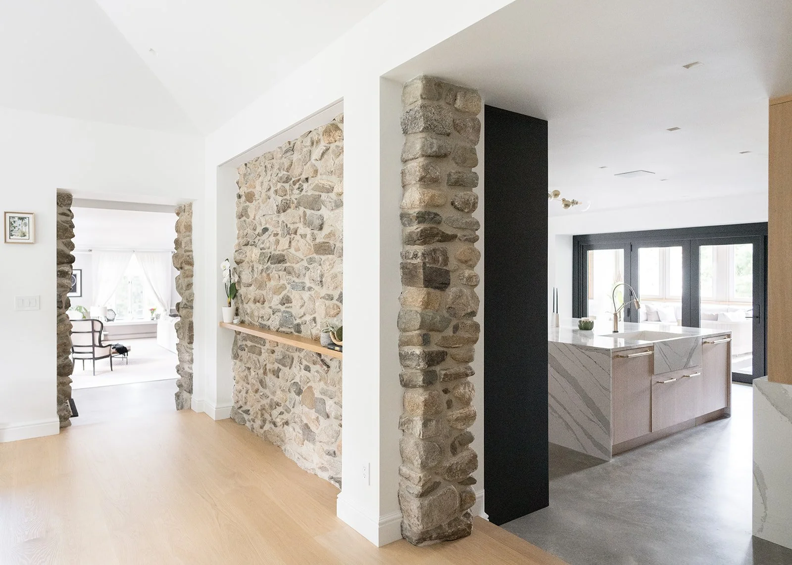 Interior view of a modern home with stone accents, a kitchen island with marble countertop, and large windows.