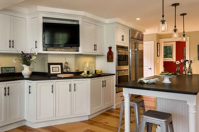 Kitchen with white cabinets, black countertops, a TV, a built-in oven, a refrigerator, and a kitchen island with bar stools.