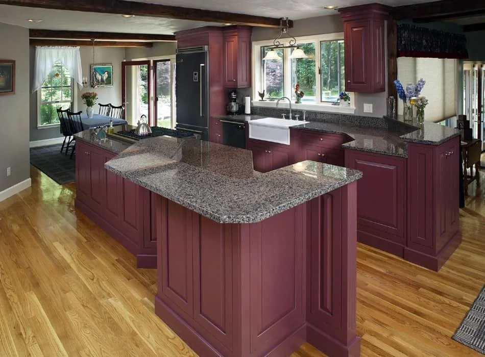 Kitchen with purple cabinets, granite countertops, a farmhouse sink, and hardwood flooring. Adjacent dining area with a table, chairs, and windows showing greenery outside.