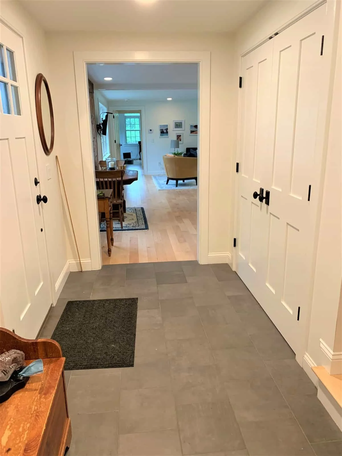 View from a tiled entryway looking into a bright living room with hardwood floors, a dining area, and a window with a view outside.