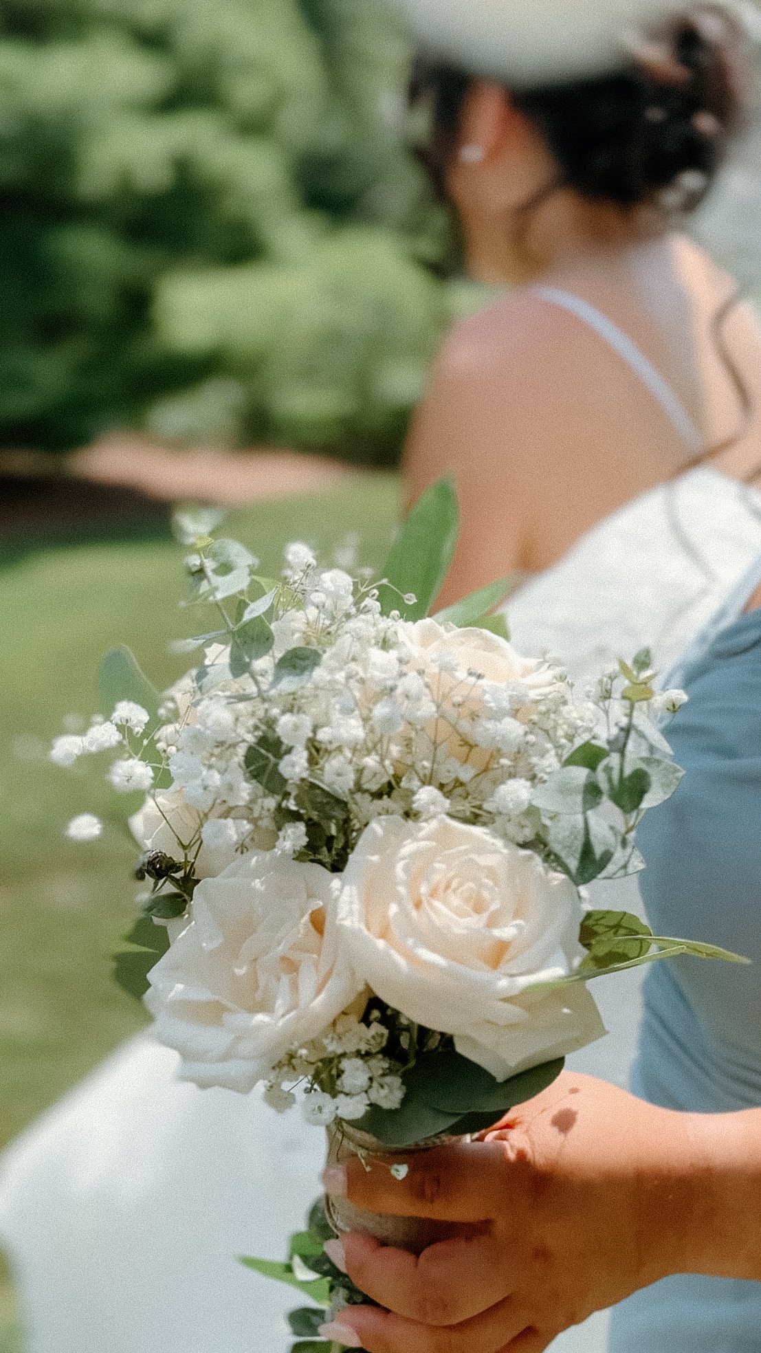 Person holding a bouquet of white roses and baby's breath flowers during a wedding ceremony.