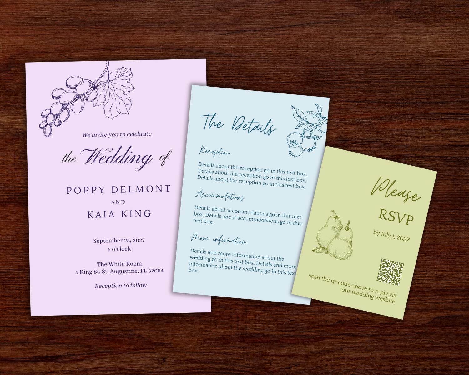 Set of three wedding invitations on a wooden surface: a lavender invite with a grapevine illustration, a blue invite with a berry illustration, and a green RSVP card with a pear illustration.