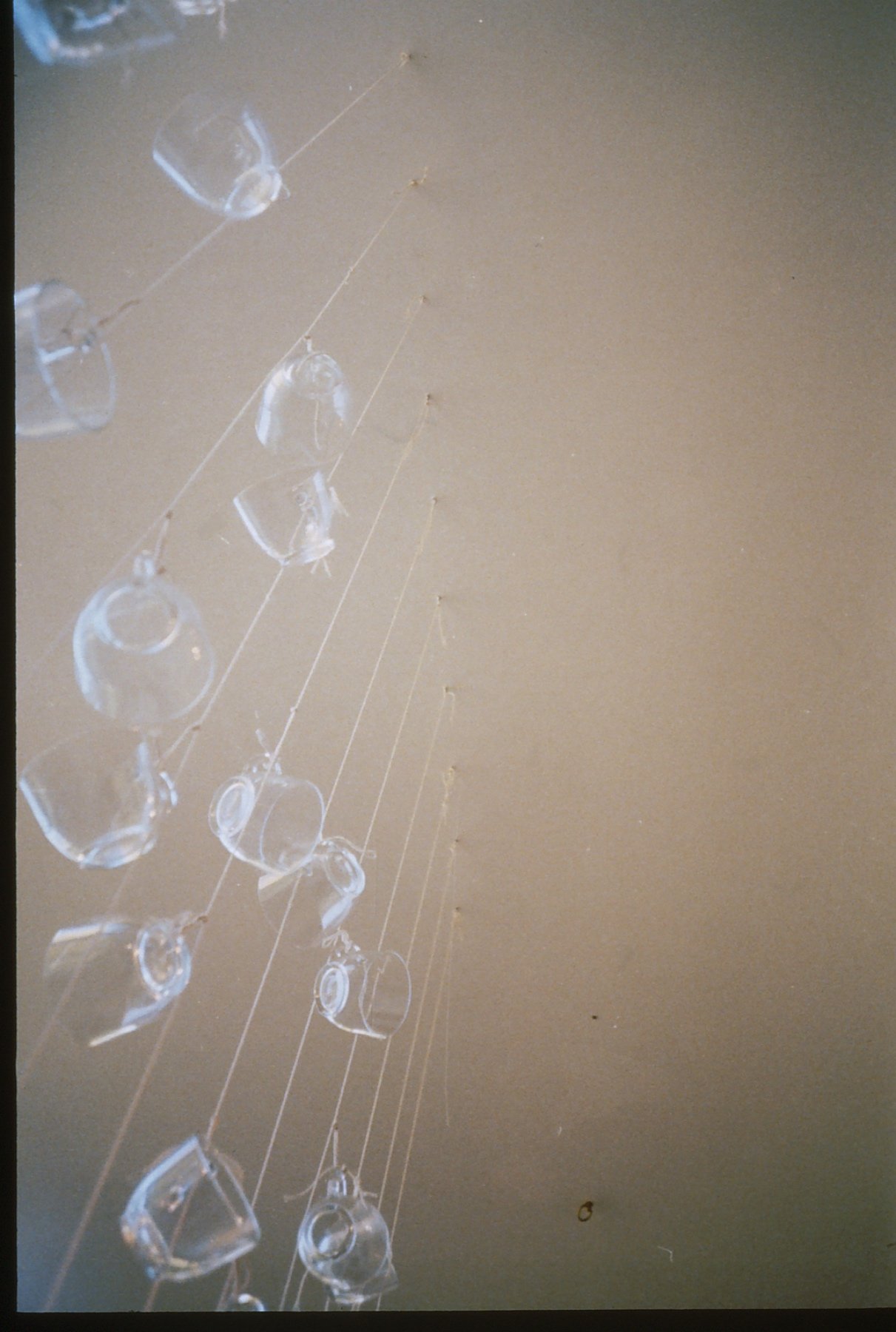 Close-up of a glass art installation with transparent glass pieces hanging from thin wires against a plain background.