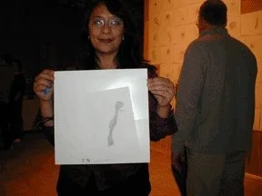 Person holding a piece of paper with a drawing of a snake, smiling and wearing glasses