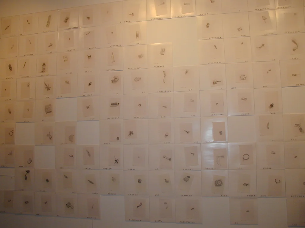 A wall covered with small paper cards arranged in a grid pattern. Each card contains a tiny, detailed drawing or object, with some cards containing words or numbers.