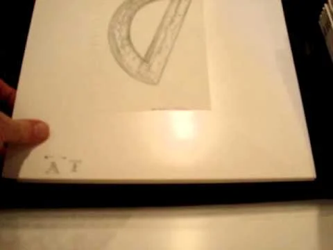 Close-up of a book page showing a geometric drawing of a 3D shape, possibly a torus or U-shaped object, with a person's hand holding the page.
