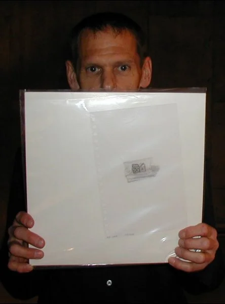 A man with short hair holding a large vinyl record album cover in front of his face.