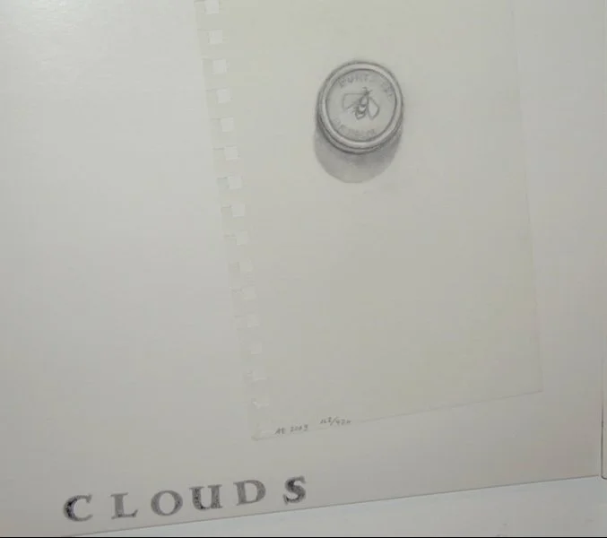 A piece of paper with the word 'CLOUDS' written on it and a small container or lid with a leaf symbol on it placed on top of the paper.