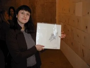 A woman holding a framed photograph indoors with a wooden wall in the background.