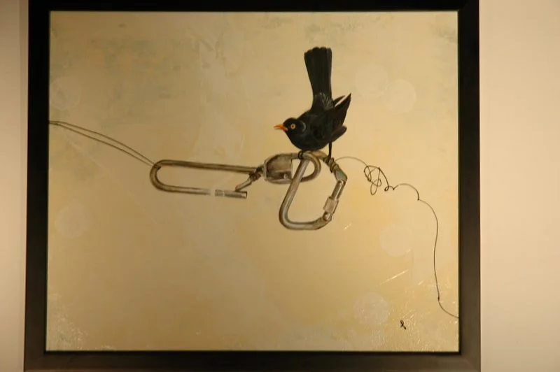 A framed artwork depicting a bird perched on a large screw, with the screw integrated into a fabric-like structure, and a wire attached to it.