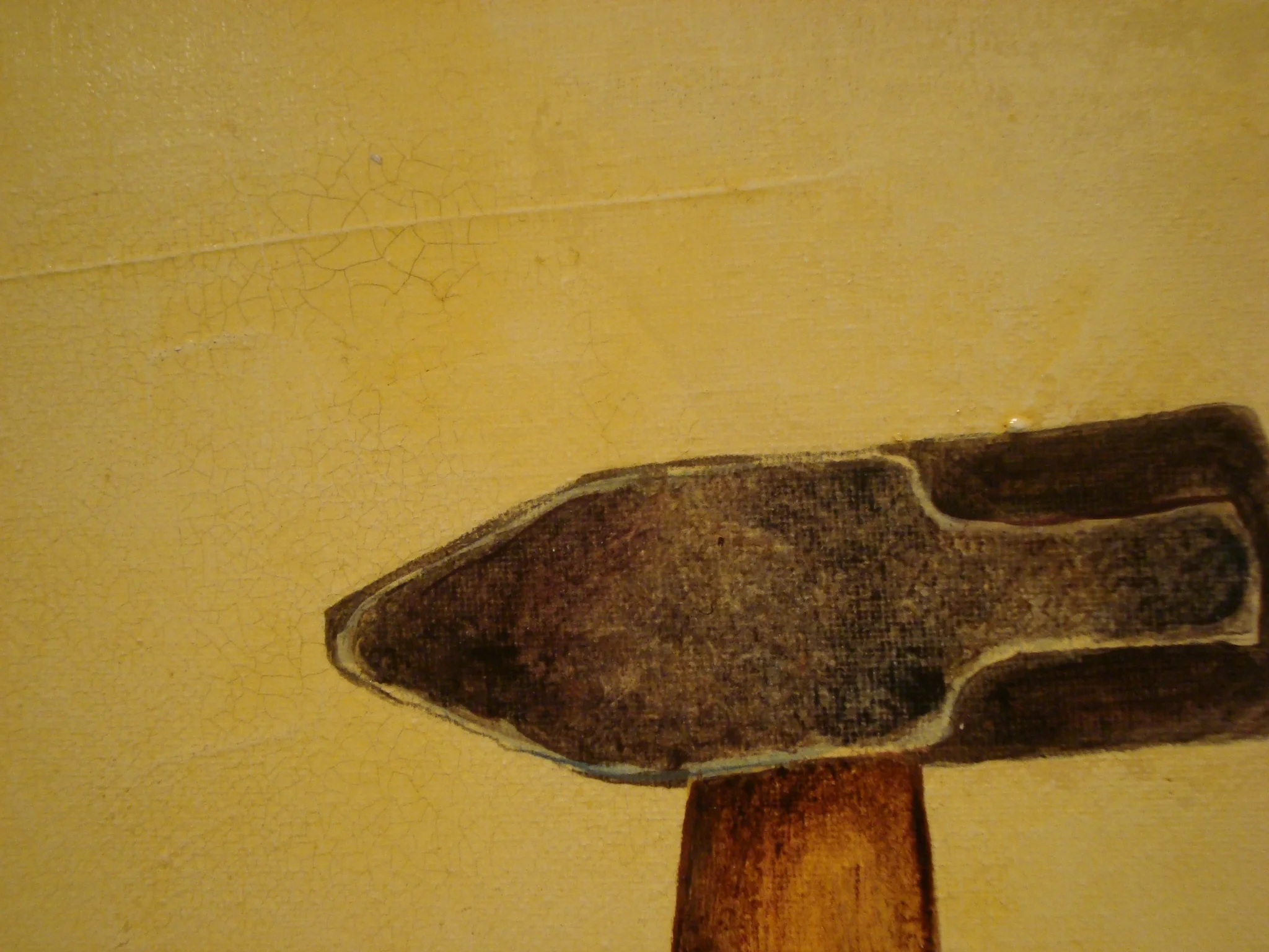 A close-up of a worn, dark-colored axe head attached to a wooden handle, resting against a yellow, textured wall with visible cracks.