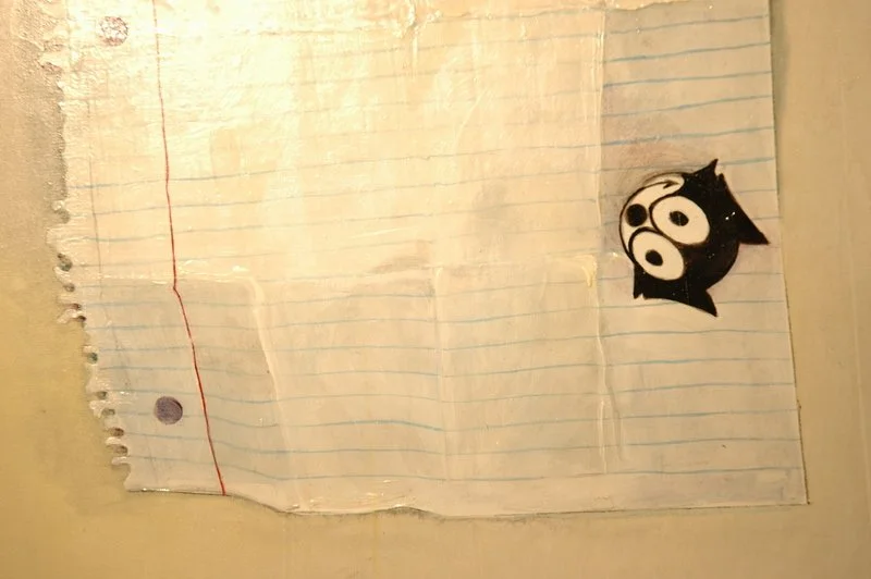 Worn, torn lined notebook page with a cartoon black cat sticker in the bottom right corner.