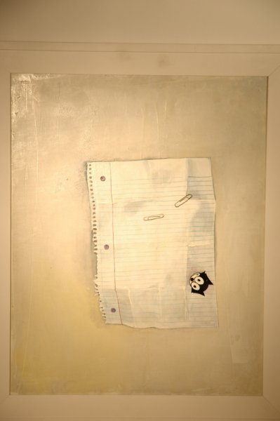 A torn sheet of lined notebook paper with a small black sticker of an owl attached to it, taped to a plain wall.