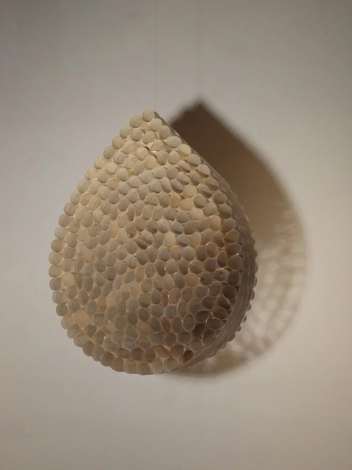 Spherical art piece made of numerous small, white, textured balls, casting a shadow on the wall.