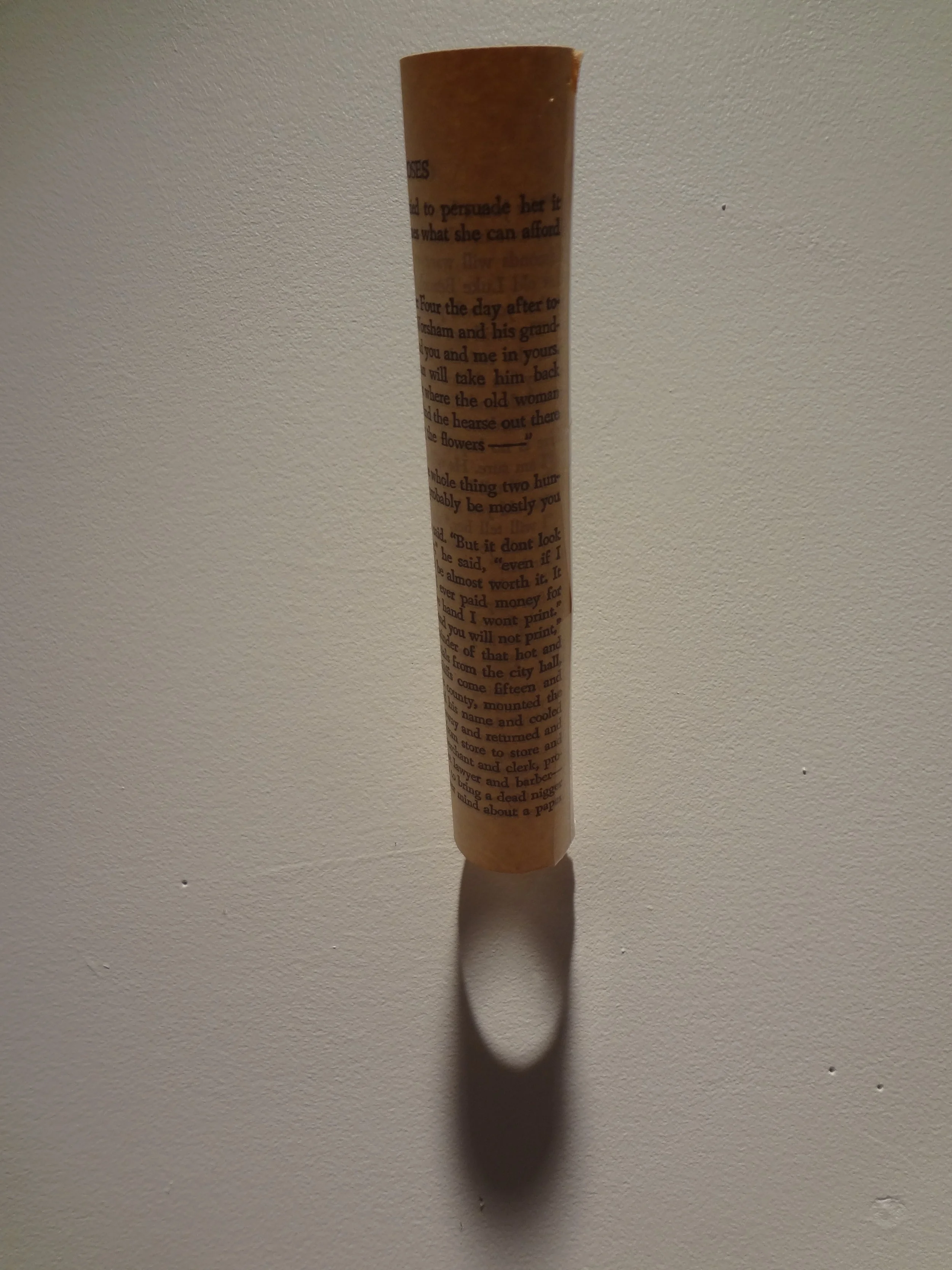 A cylindrical object with printed text standing upright on a white surface, casting a shadow.