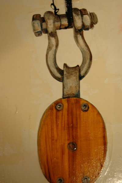 Close-up of a metal hook connected to a wooden base with screws, mounted on a wall.