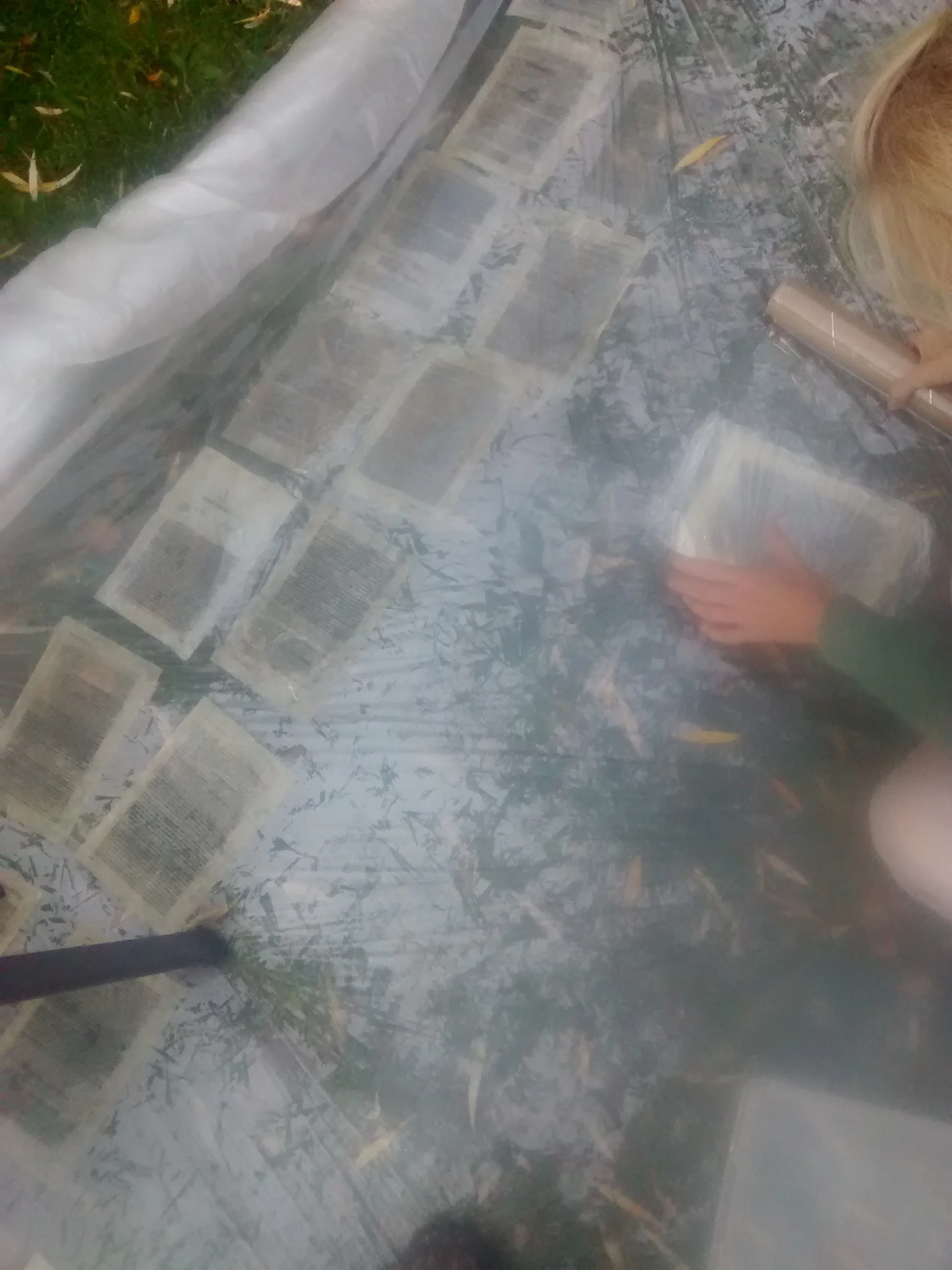 People are outside reading newspapers on a plastic-covered surface.