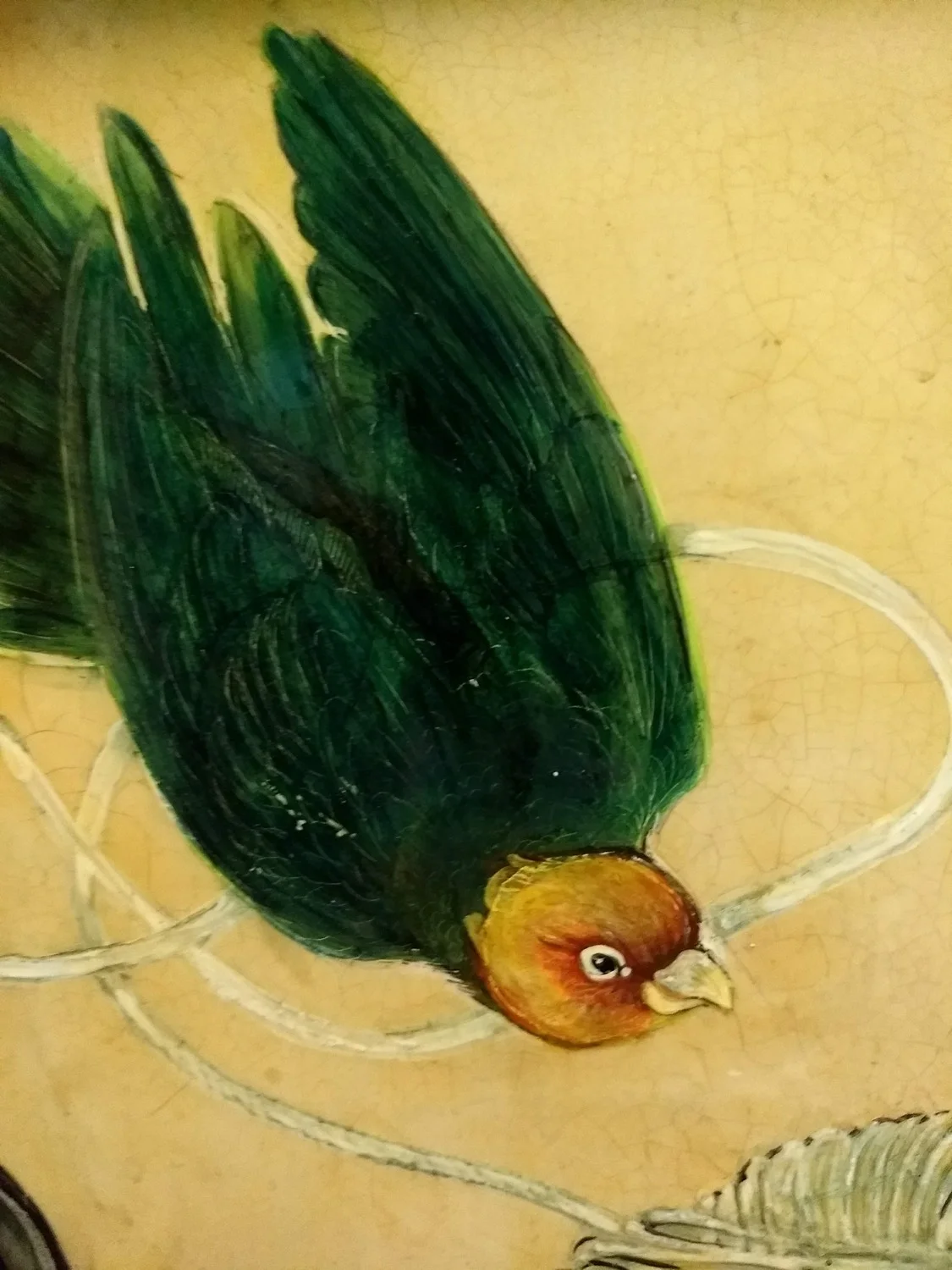 Painting of a bird with a brown head and green body, lying upside down on a yellowish background.