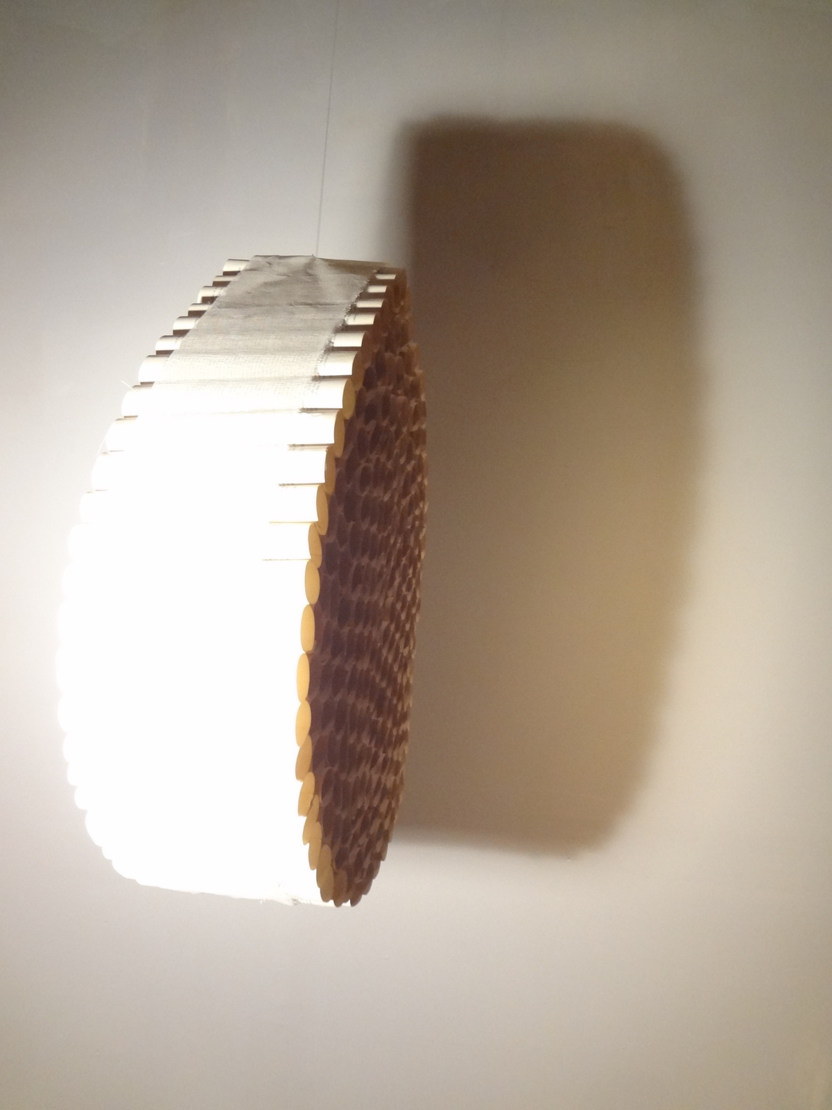 A round, wooden wall lamp casting a shadow on the ceiling.