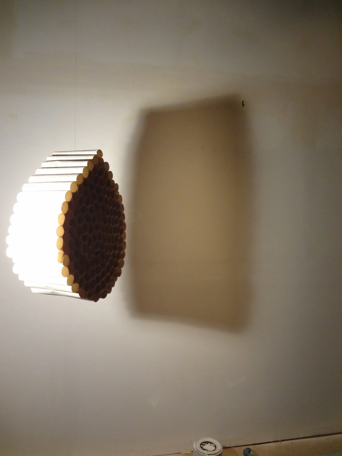 Light fixture made of stacked pencils casting a shadow on the wall.