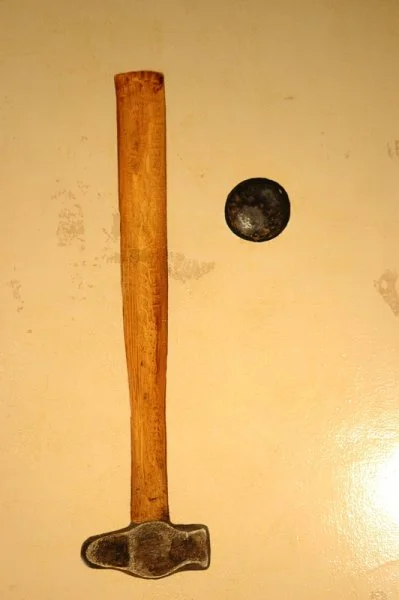 A wooden hammer with a metal head and a black ball-shaped object on a light-colored surface.