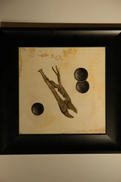 An abstract artwork featuring a wooden figure, possibly a rabbit or hare, with geometric black circles on a beige background, framed in black.