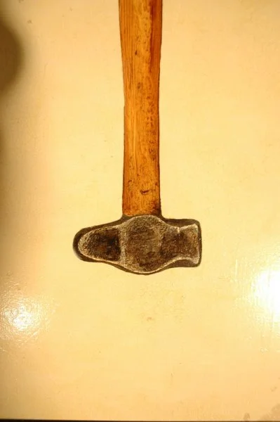 A hammer with a wooden handle and a metal head resting on a light-colored surface.