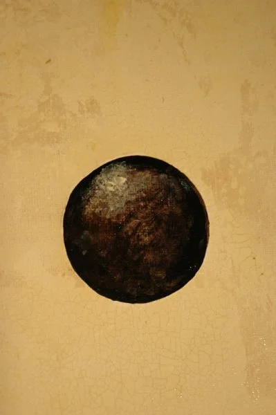 A black circular object on a yellowish textured surface.
