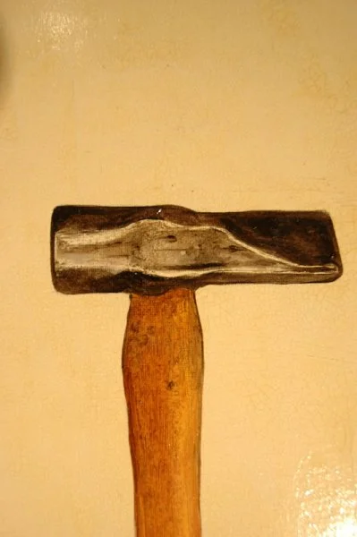 A hammer with a wooden handle and a metal head against a beige wall.