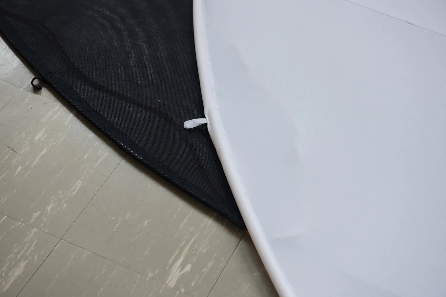 Close-up of a black mesh bag or case on beige tiled floor, partially visible, with a white foam or plastic object resting on top.