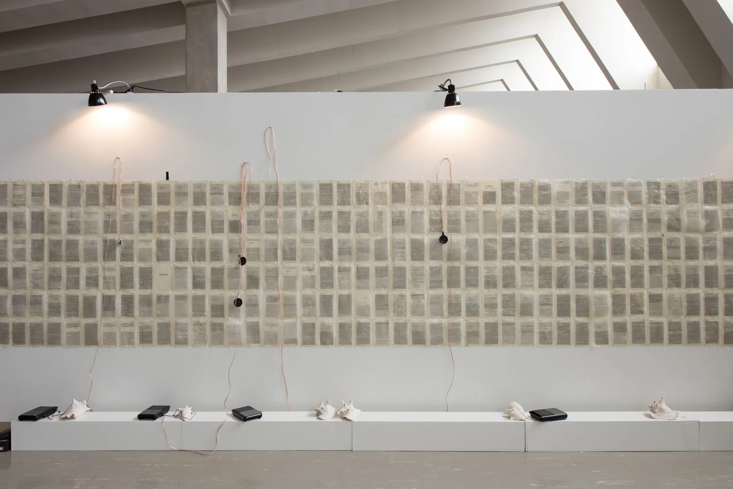 Contemporary art installation with a wall of shells, electronic devices, and wires in a modern gallery space.