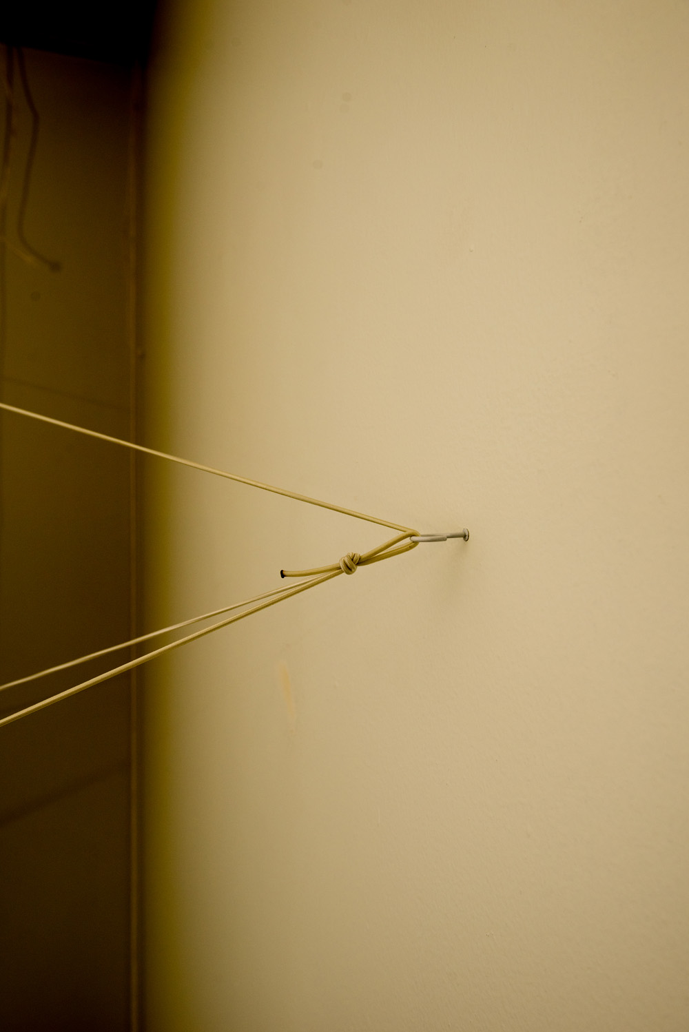 A beige wall with a metal hook and a hanging cord tied in a knot