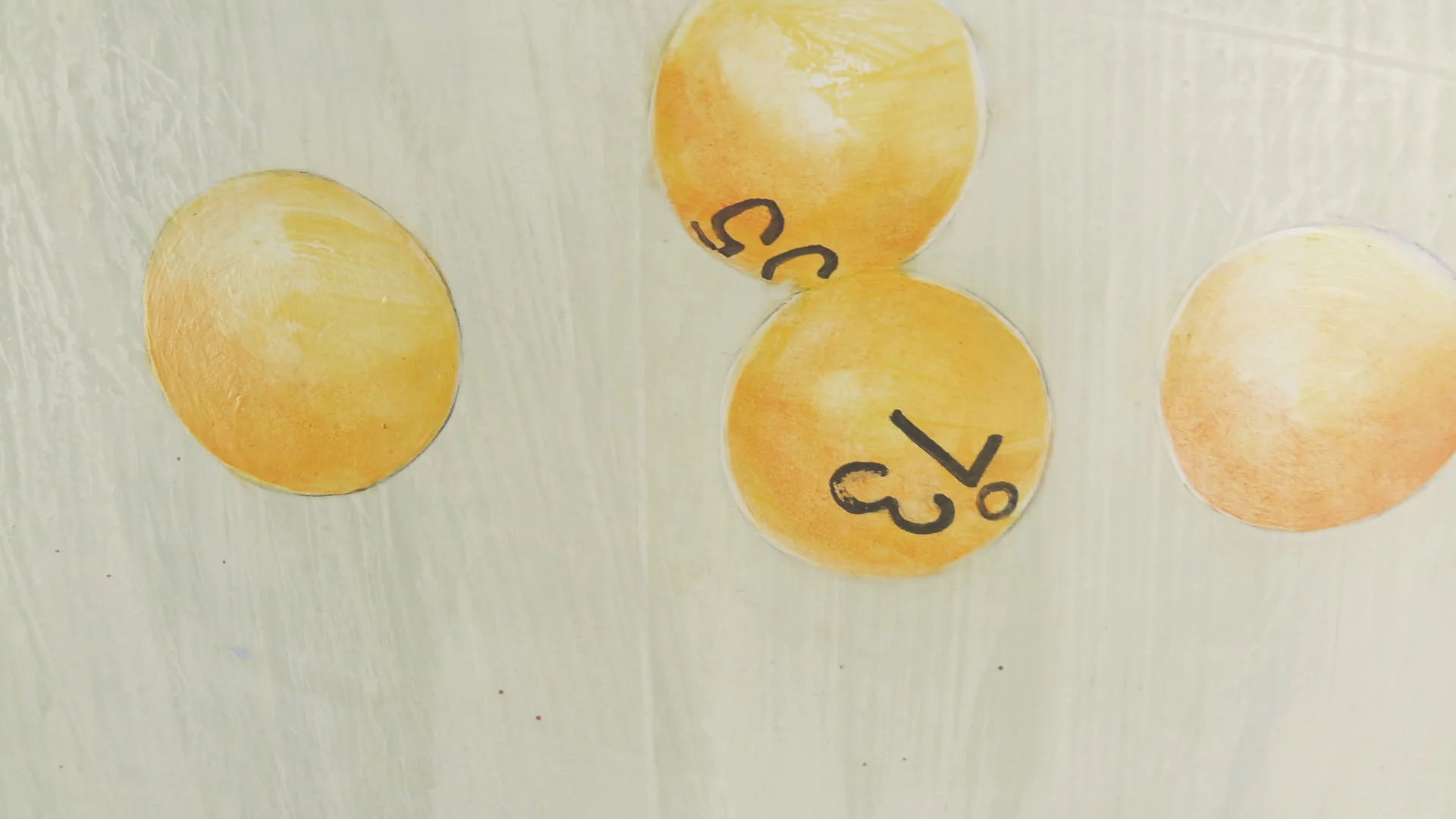 Four yellow-orange circular stickers with black doodle markings on a light-colored wooden surface.