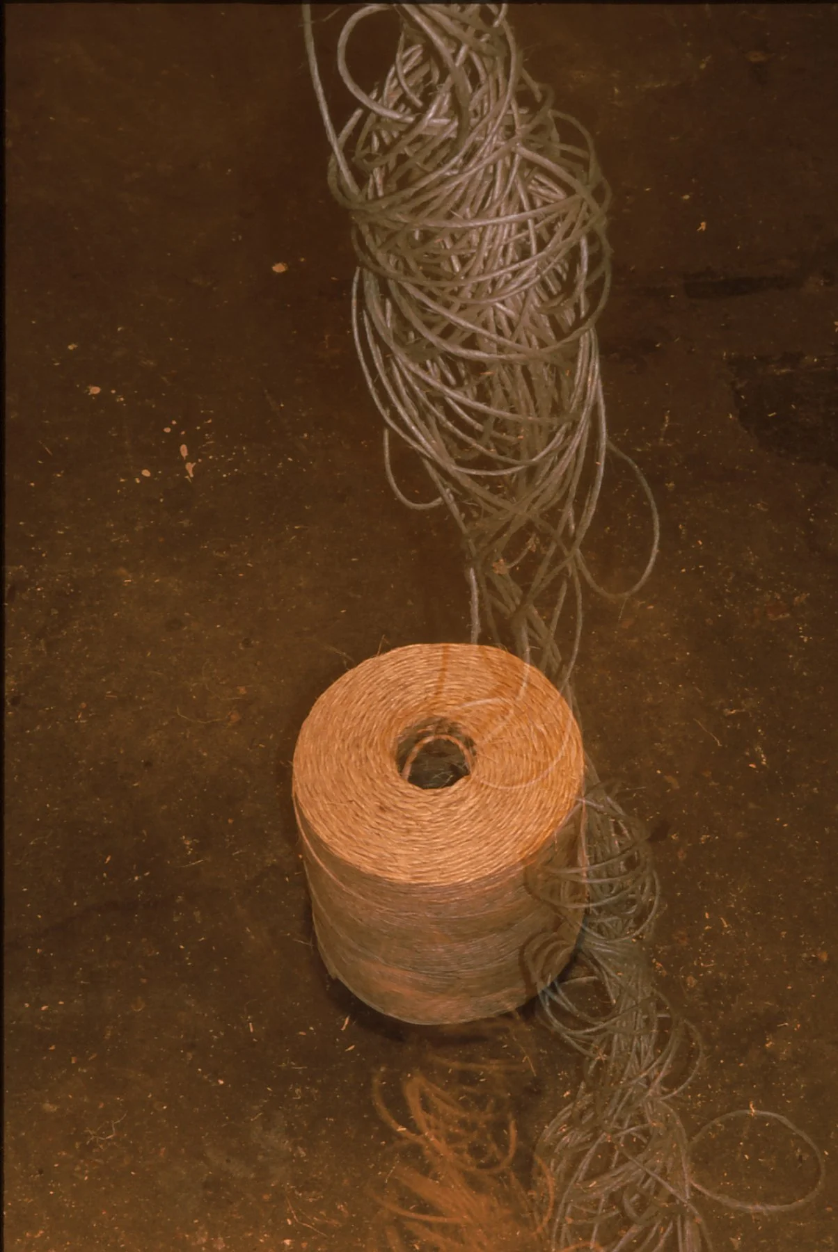 A wooden table with a large spool of wire and a stack of woven wire rods, with a long, coiled wire extending from the spool.