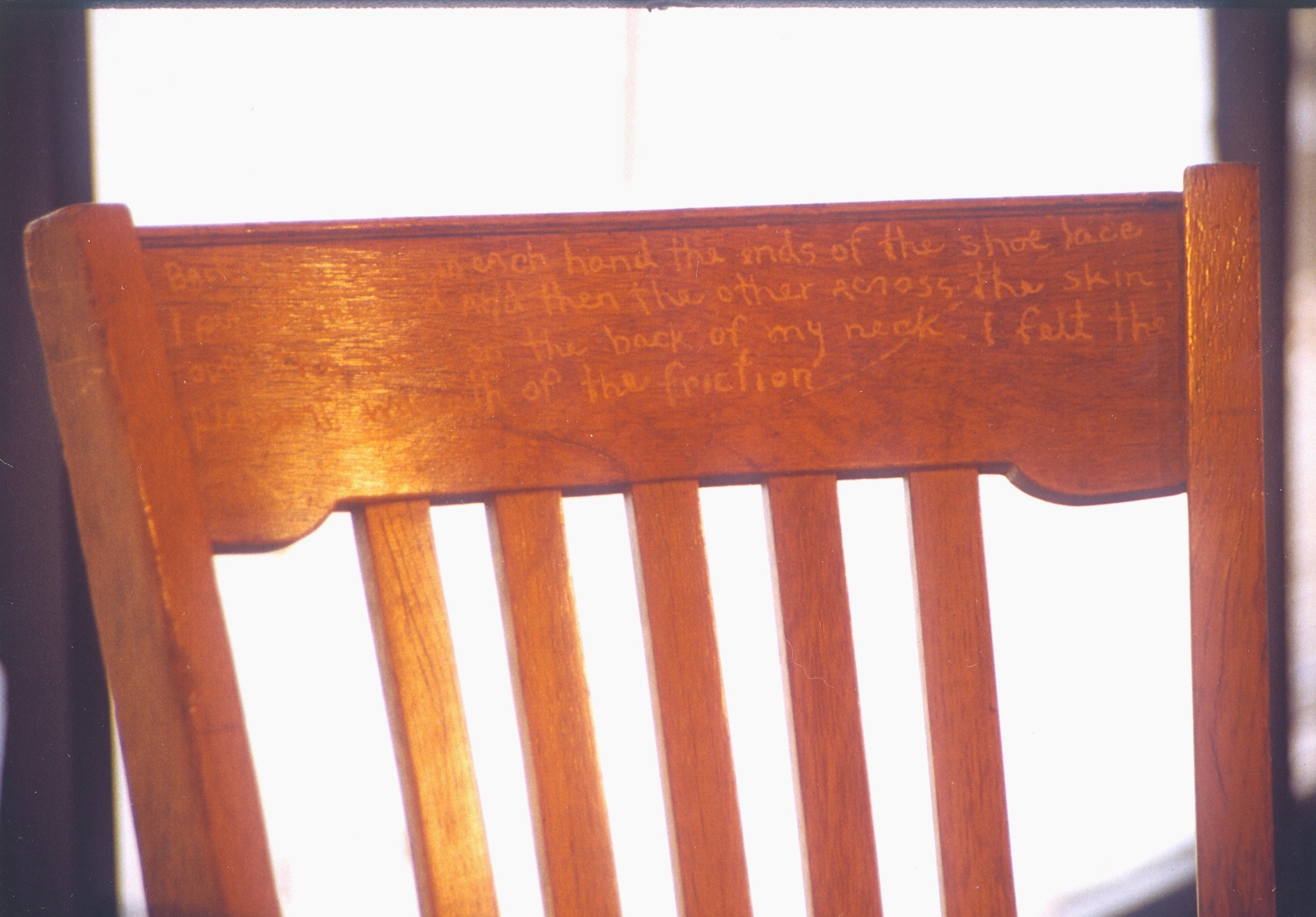 Wooden chair with a handwritten message inscribed on the top rail backrest.