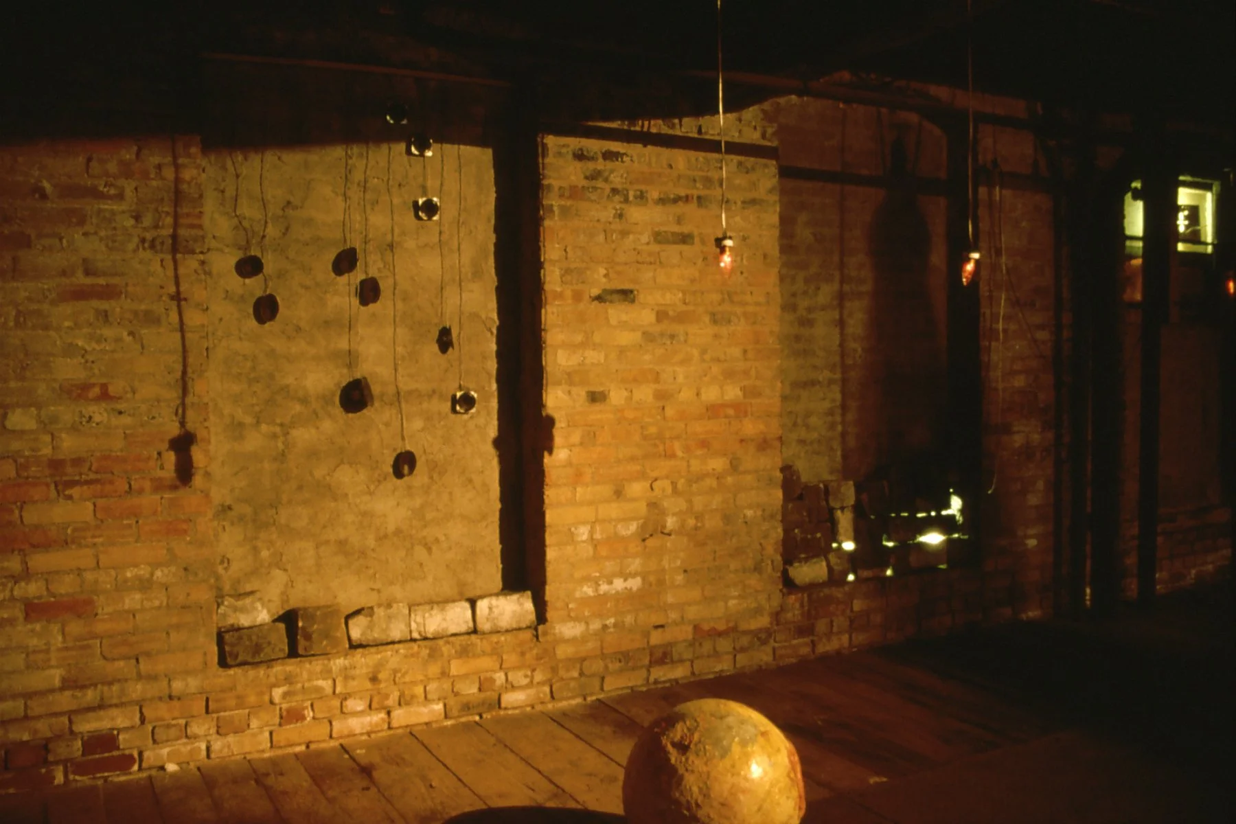 Dimly lit brick wall interior with hanging string lights and a large spherical object on the floor.