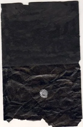 A crumpled piece of black paper or fabric with a small shiny, reflective object in the center.