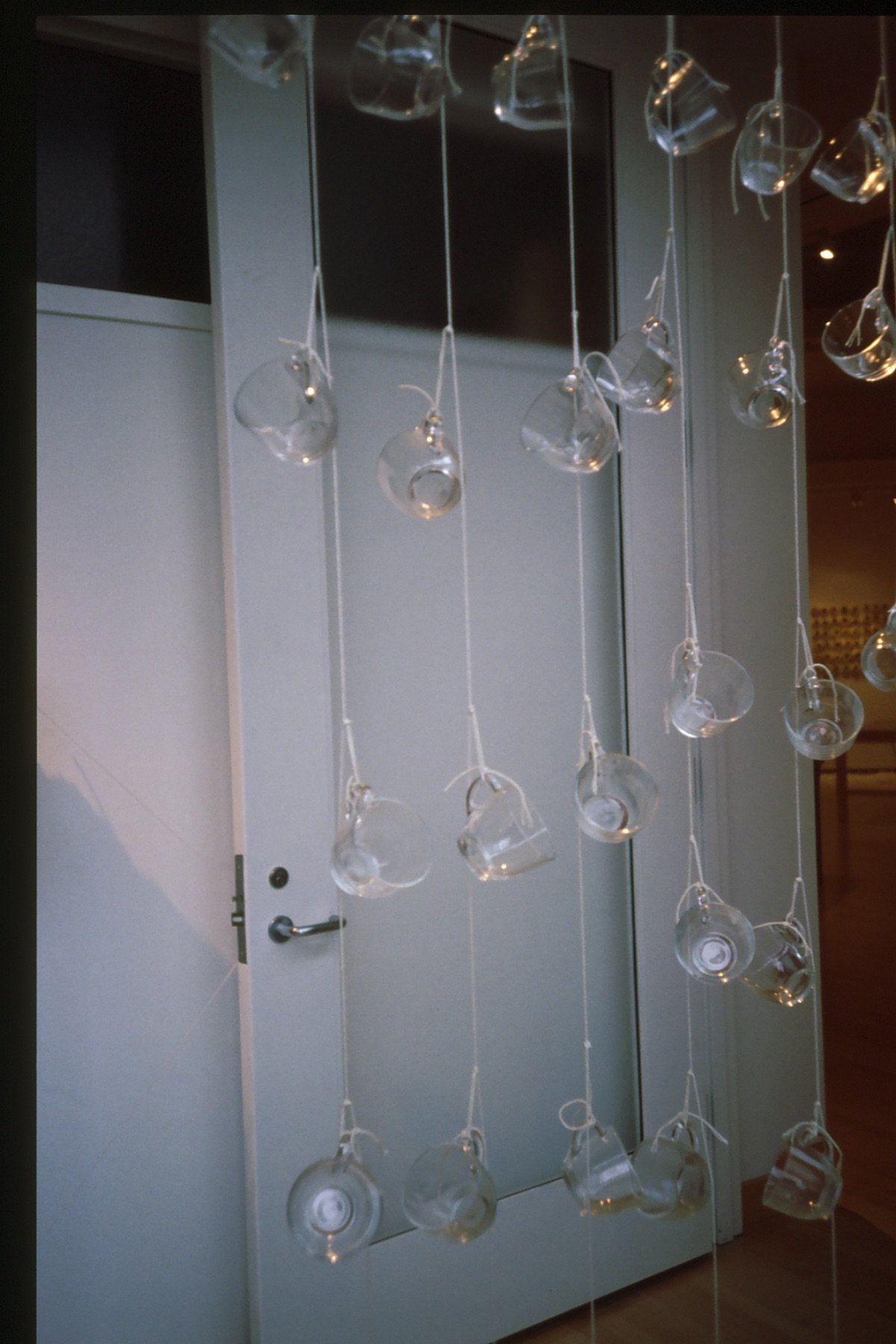 Hanging strings of empty glass cups tied with white string in front of a closed door.