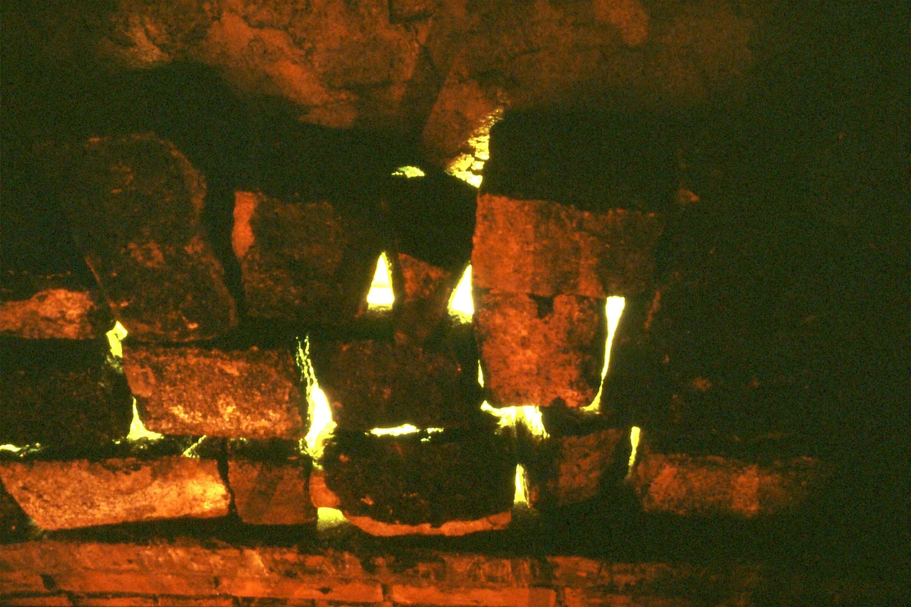 A close-up view of a brick fireplace with flames visible through gaps in the bricks.
