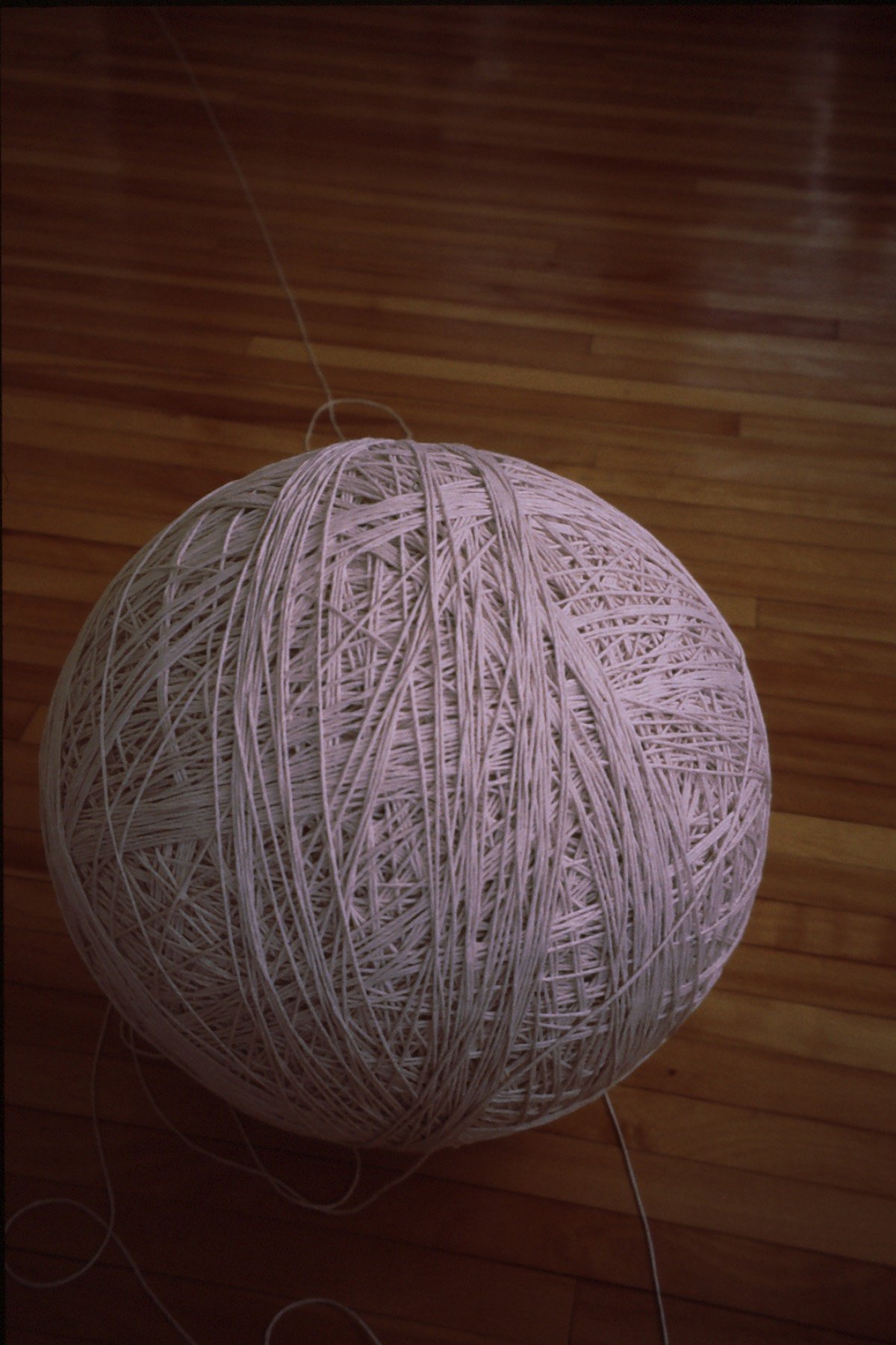A spherical ball of tangled white string or yarn on a hardwood floor.