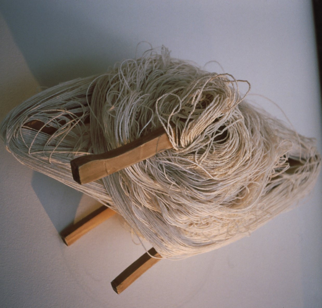 A woven chair with a wooden frame and tangled string or yarn resting on it.