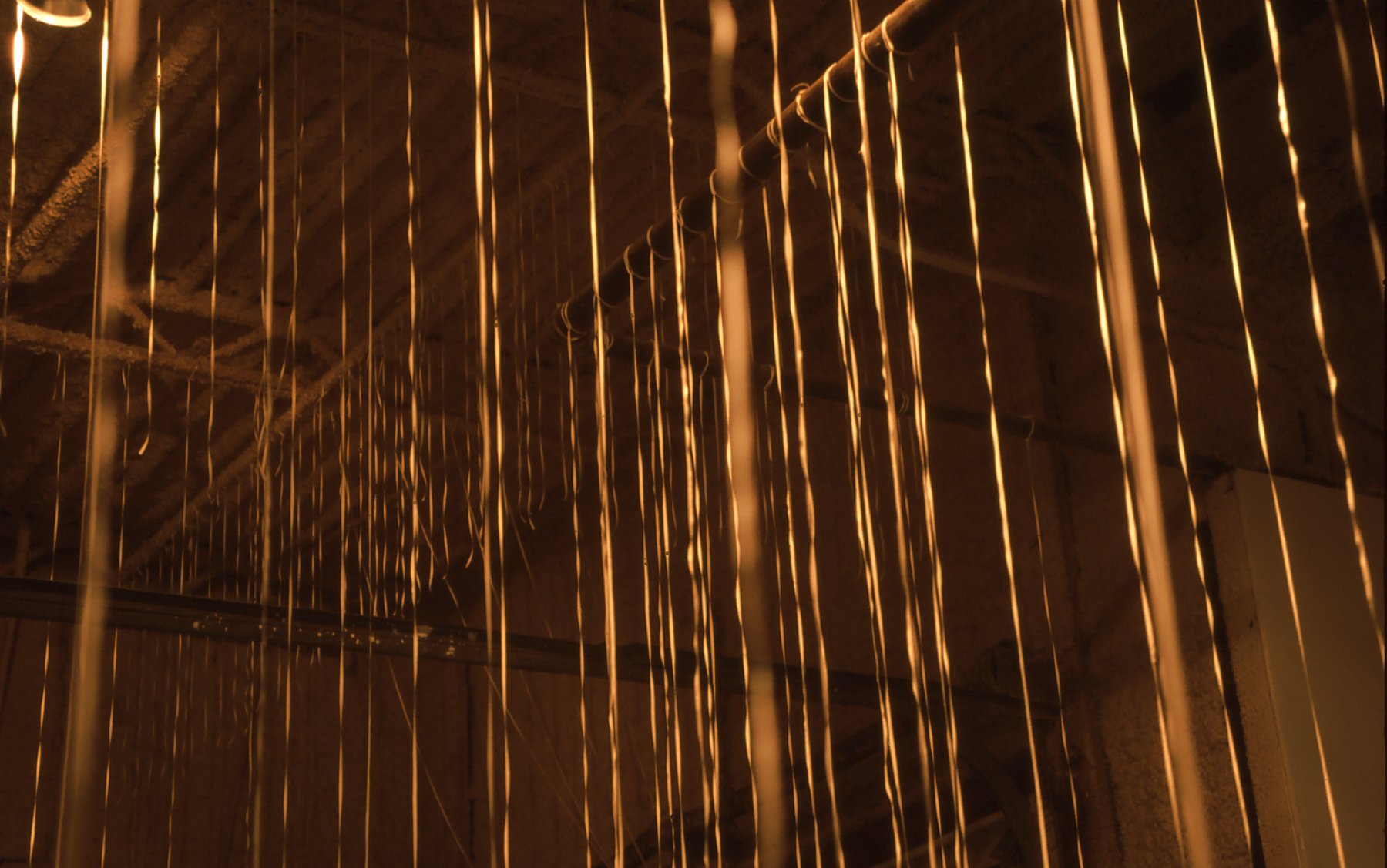 Close-up view of metallic lightning rods hanging vertically from a ceiling, reflecting warm light in an industrial setting.